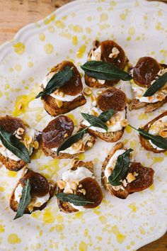 a white plate topped with toasted bread covered in cream cheese and sage leaf toppings