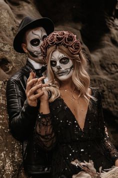 a man and woman dressed up in skeleton makeup, holding hands to each other while standing next to some rocks