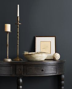 a wooden table with a bowl and candles on it next to a framed photograph, candle holder and other items