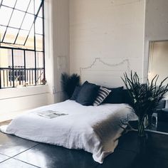 a white bed sitting next to a window with black pillows and blankets on top of it