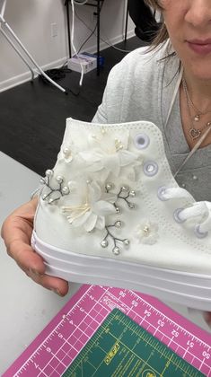 a woman holding up a shoe with flowers on the side and buttons in the bottom