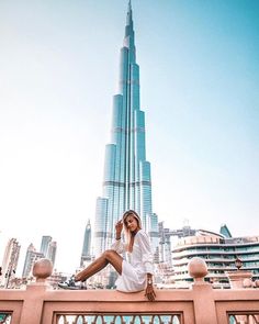 a woman is sitting on a ledge in front of the burj building, talking on her cell phone