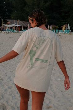 Model posing at the beach from the back, showing her t-shirt with mermaid illustration Summer Organic Cotton T-shirt, Organic Cotton Summer T-shirt, Unisex Organic Cotton T-shirt For Summer, Relaxed Short Sleeve T-shirt For Relaxation, Relaxed Summer T-shirt For Relaxation, Organic Cotton Crew Neck T-shirt, Relaxed Fit Conscious Style T-shirt For Everyday, Summer Cotton Tops With Back Print, Cotton Tops With Back Print For Summer