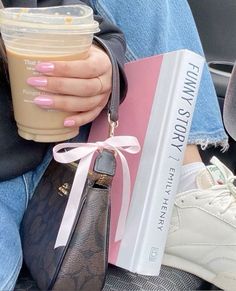 a person holding a book and a drink in their hand while sitting on a car seat