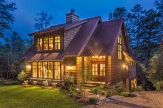 a large wooden house lit up at night with lights on the windows and shingled roof