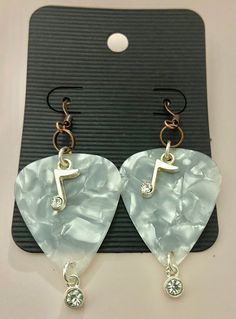 a pair of guitar pick earrings with swarong crystals on them sitting on top of a black card board