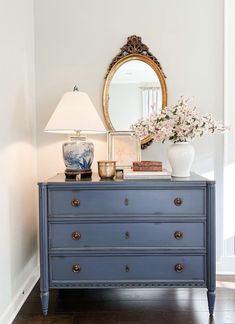 a blue dresser with flowers on top and a mirror in the corner next to it