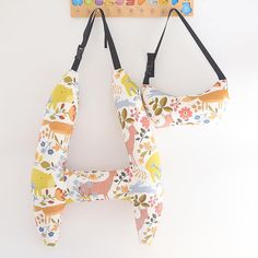 two children's toys hanging from hooks on a white wall with flowers and animals