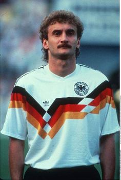 a man with a mustache standing in front of a soccer field wearing a striped shirt