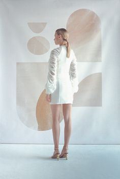 a woman standing in front of a wall with an abstract painting on it's side