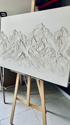 a white canvas with mountains drawn on it in front of a easel and paintbrush