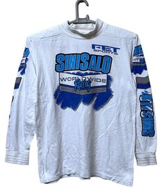 a white long sleeve shirt with blue and grey lettering on the chest, in front of a hanger