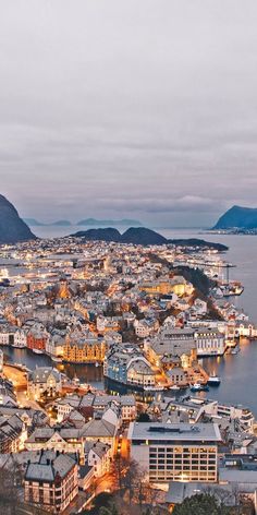 an aerial view of a city at night with mountains in the background and boats on the water