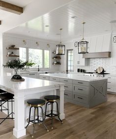 a large kitchen with white cabinets and wooden flooring, along with two bar stools