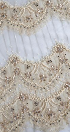 an embroidered lace with beading and pearls on white fabric, close - up view