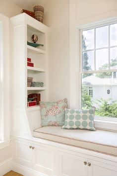 a window seat in the corner of a room with pillows on it and bookshelves