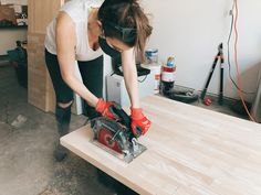 a woman using a circular saw to cut wood with a mitt on the table