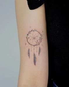 a woman's arm with a small dream catcher tattoo on it