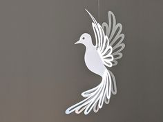 a white paper bird hanging from a string on a gray wall next to a clock