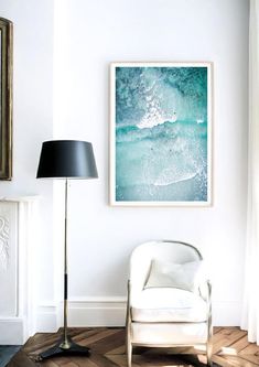 a living room with a white chair and a painting on the wall next to a lamp