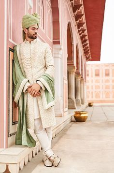 a man in a white and green outfit leaning against a wall with his hands on his hips