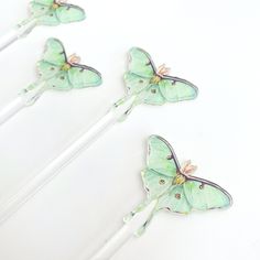 three green butterflies sitting on top of white sticks