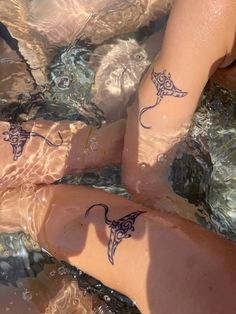 two people are sitting in the water with tattoos on their legs