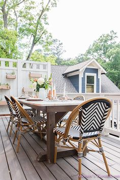 an outdoor table and chairs on a wooden deck with white picket fence in the background