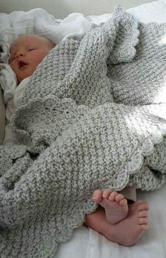 a baby wrapped up in a blanket on top of a white bed with its feet tucked under the covers