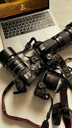 a laptop computer sitting on top of a white table next to cameras and a camera strap