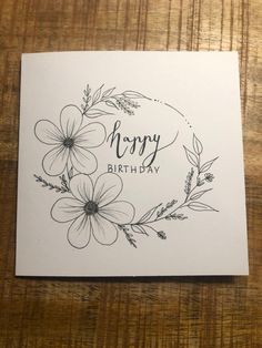 a happy birthday card with flowers and leaves on the front, sitting on a wooden table