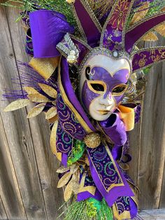 a purple mask with green and gold decorations on it's face is hanging from a wooden fence