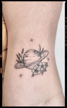 a small saturn tattoo on the side of a woman's stomach, with flowers around it