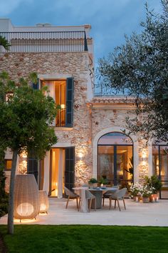 an outdoor dining area in front of a stone building at night with lights on the windows