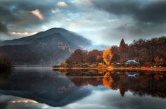 a lake surrounded by trees and mountains under a cloudy sky