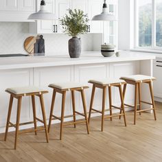 three stools in front of a white kitchen island with potted plant on it