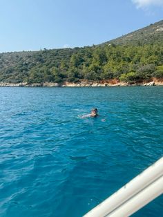 a person swimming in the ocean near some trees and mountains on a sunny day with clear blue water