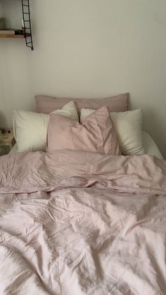 an unmade bed with pink sheets and white pillows in a small bedroom area next to a book shelf