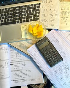 a laptop computer sitting on top of a desk covered in papers and fruit next to a calculator