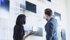 two people standing in front of a wall holding cell phones and looking at each other