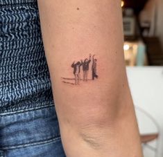 a woman's arm with a small tattoo of three people standing on the beach