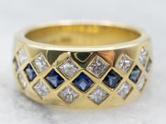 This sapphire and diamond-encrusted band makes a bold statement! Sparkling from every angle, the deep navy gems contrast beautifully with the bright, glittering diamonds, creating an elegant pattern on the ring. Versatile and glamorous, this piece would make a stunning anniversary ring!Metal: 18K Yellow GoldGem: 7 Sapphires Gem Measurements: 2.0 mm, SquareAccents: 12 Diamonds totaling .70 Carats, H in Color, VS in ClarityWidth of Band: 8.9 mmHeight off Finger: 2.7 mmRing Size: 6.25Marks: "(C) cordova 18K" Stamped on the inside band Sapphire And Diamond Band, Sapphire Band, White Gold Sapphire, Gold Cufflinks, Elegant Pattern, Diamond Glitter, Square Rings, Diamonds And Gold, White Gold Band