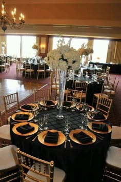 a table set up with black linens, gold chargers and white flower centerpieces