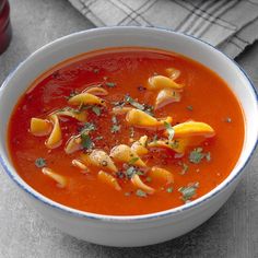 a bowl of tomato soup with pasta and parsley on the top, ready to be eaten