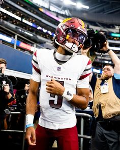 a football player is walking on the sidelines with his helmet up to his face