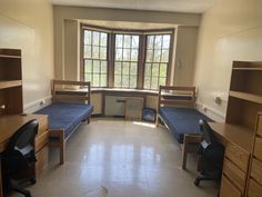 a room with three beds and two desks in front of a window that is open