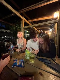 three people sitting at a table looking at their cell phones and drinking drinks in front of them