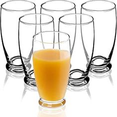 a glass filled with orange juice sitting next to four glasses on top of a white surface