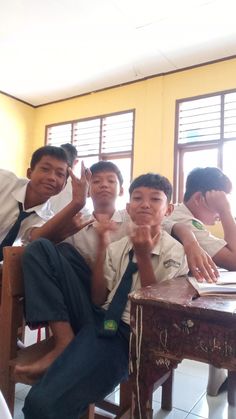 four boys sitting at desks with their hands in the air