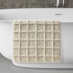 a white bath tub sitting next to a gray wall with a towel hanging from it's side